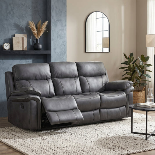 A dark gray leather reclining loveseat sofa shown in a styled living room setting with a textured rug, side table, potted plant, and wall decor.