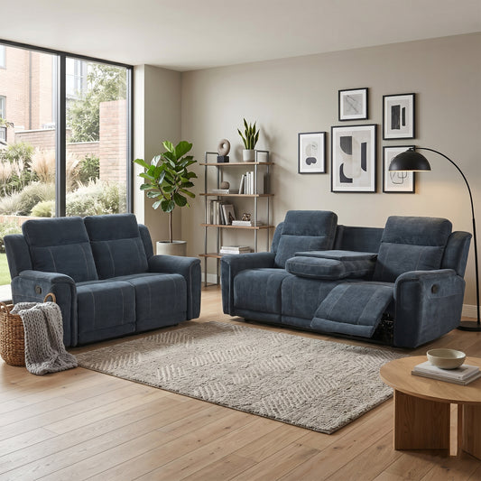 A modern living room featuring a dark blue velvet reclining loveseat and a matching two-seater sofa, styled with a textured beige rug, a wooden coffee table, and framed wall art.