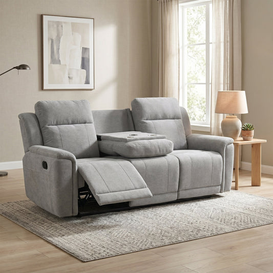 A light gray reclining loveseat sofa with a center console tray table, shown in a staged living room setting with a side table, lamp, window, and rug.